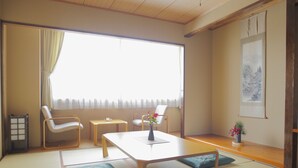 A traditional Japanese room with tatami flooring, a low table, two chairs, a small table, a vase with flowers, and a framed picture on the wall. - Centrale Hotel Kyotango (Kyotango)