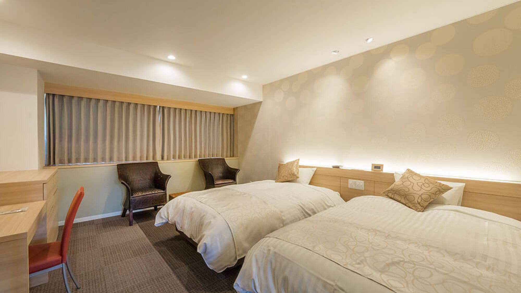 A hotel room with two beds, a desk, and a chair.