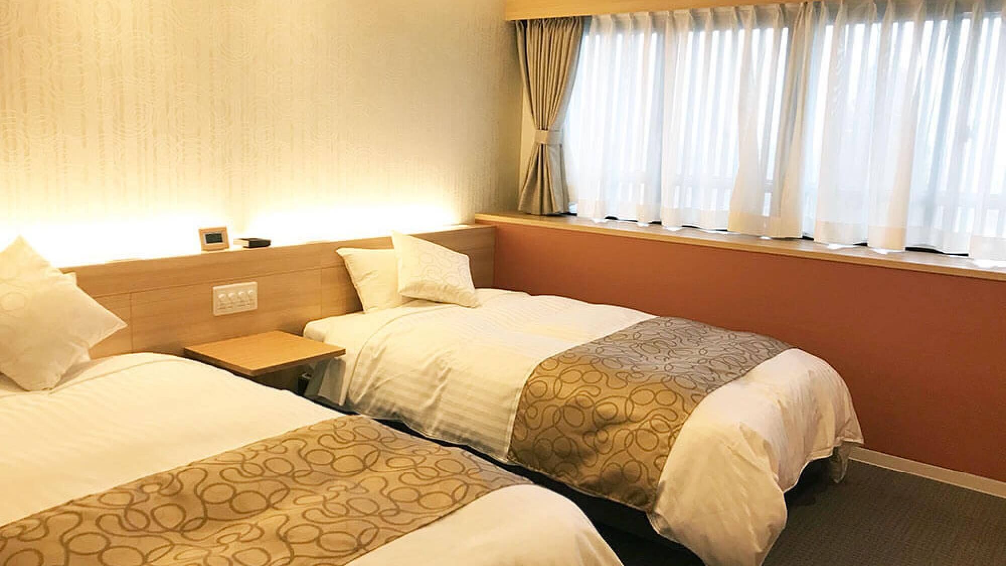 A hotel room with two beds, a nightstand, a window with curtains, and a wall-mounted control panel.