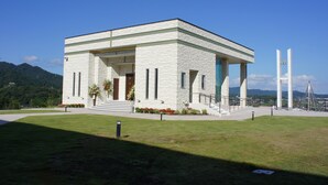 A white building with a flat roof, a front entrance, and a small garden area with flowers. - Centrale Hotel Kyotango (Kyotango)