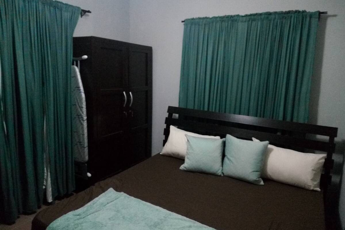 A bedroom with a bed, a wardrobe, and green curtains.