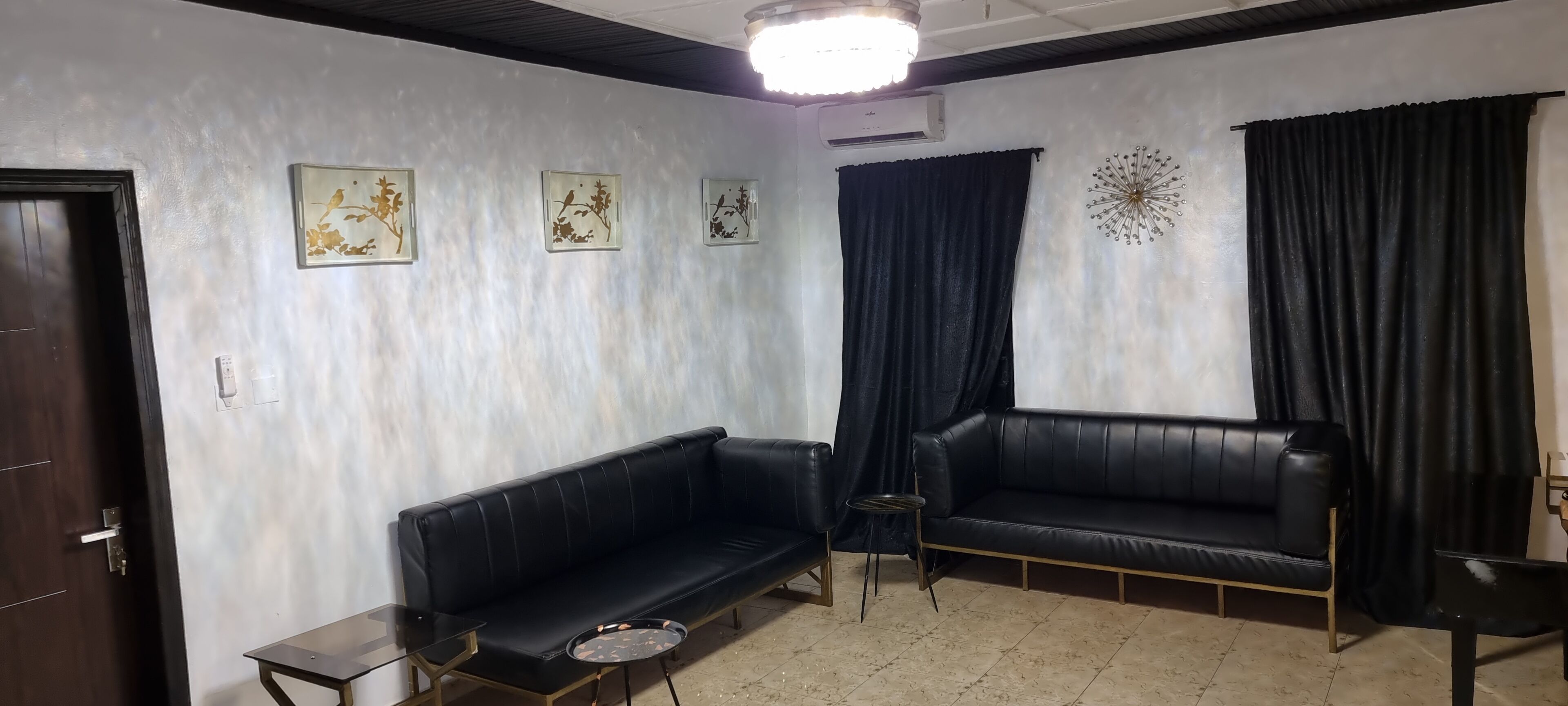 Une pièce comprenant deux canapés en cuir noir, une petite table ronde et trois œuvres d’art représentant des oiseaux, accrochées au mur.
