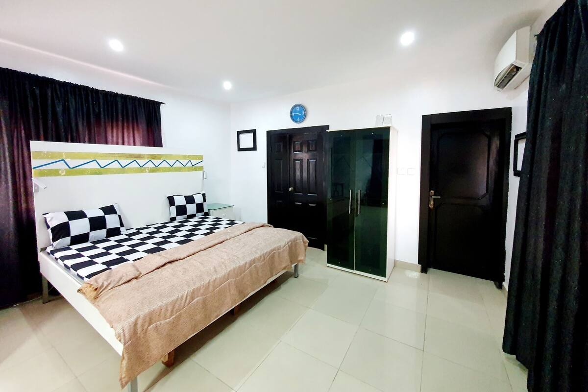 A bedroom with a bed, a wardrobe, a door, and a clock on the wall.