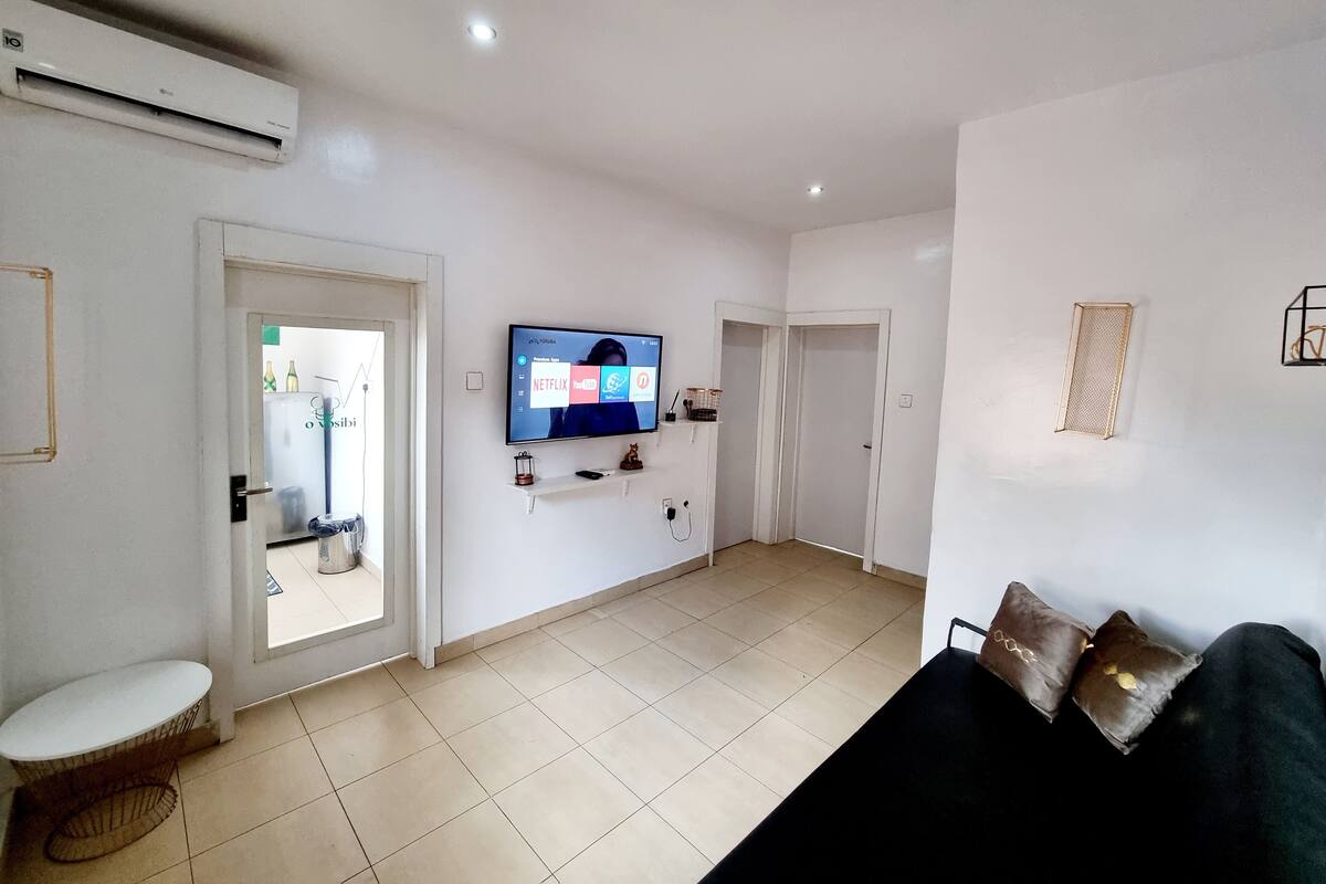 A living room with a flat-screen TV mounted on the wall, a sofa, a small table, and a door leading to another room.