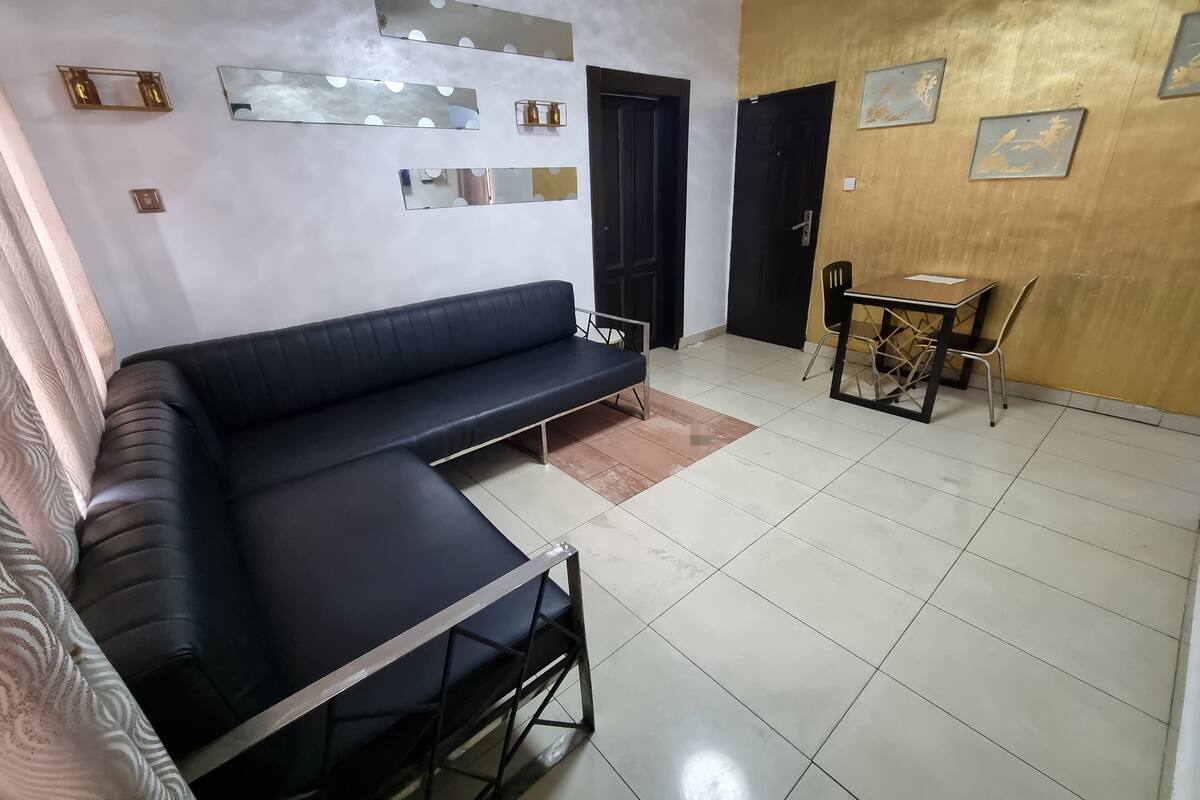 A modern living room with a black sofa, a small table with chairs, and a wall decorated with mirrors and framed pictures.