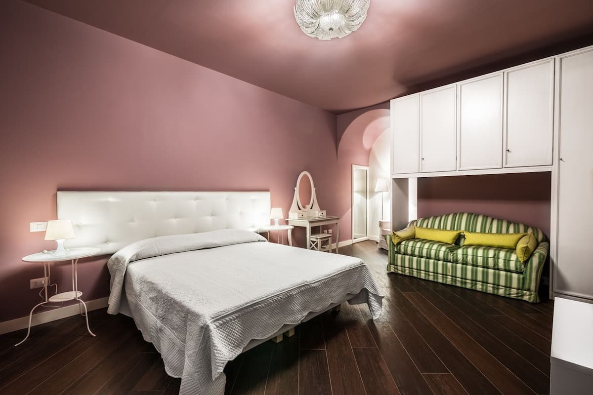 A bedroom with a large bed, a vanity with a mirror, a green-striped sofa, and white cabinets.