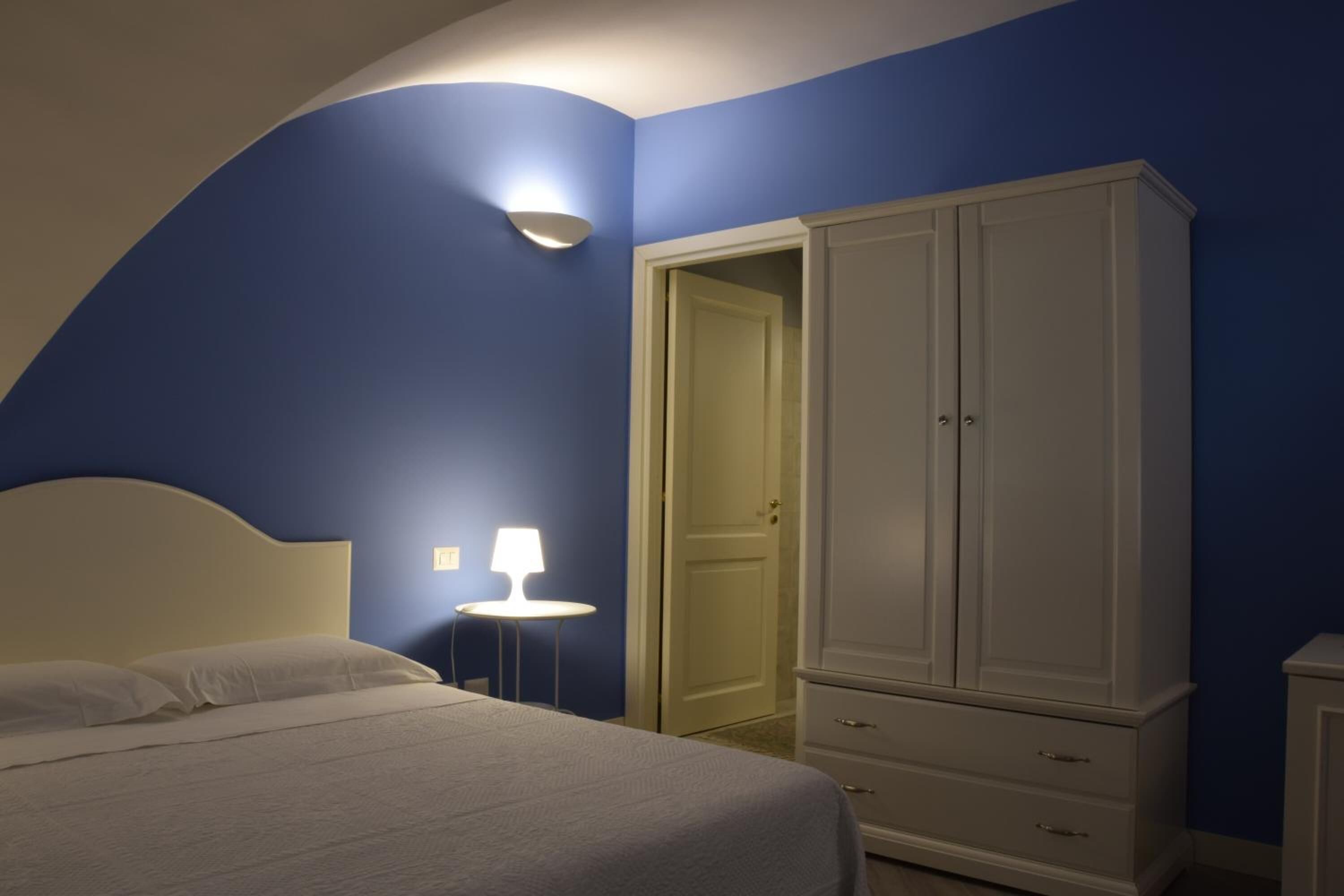 A bedroom with a bed, a wardrobe, and a nightstand with a lamp.