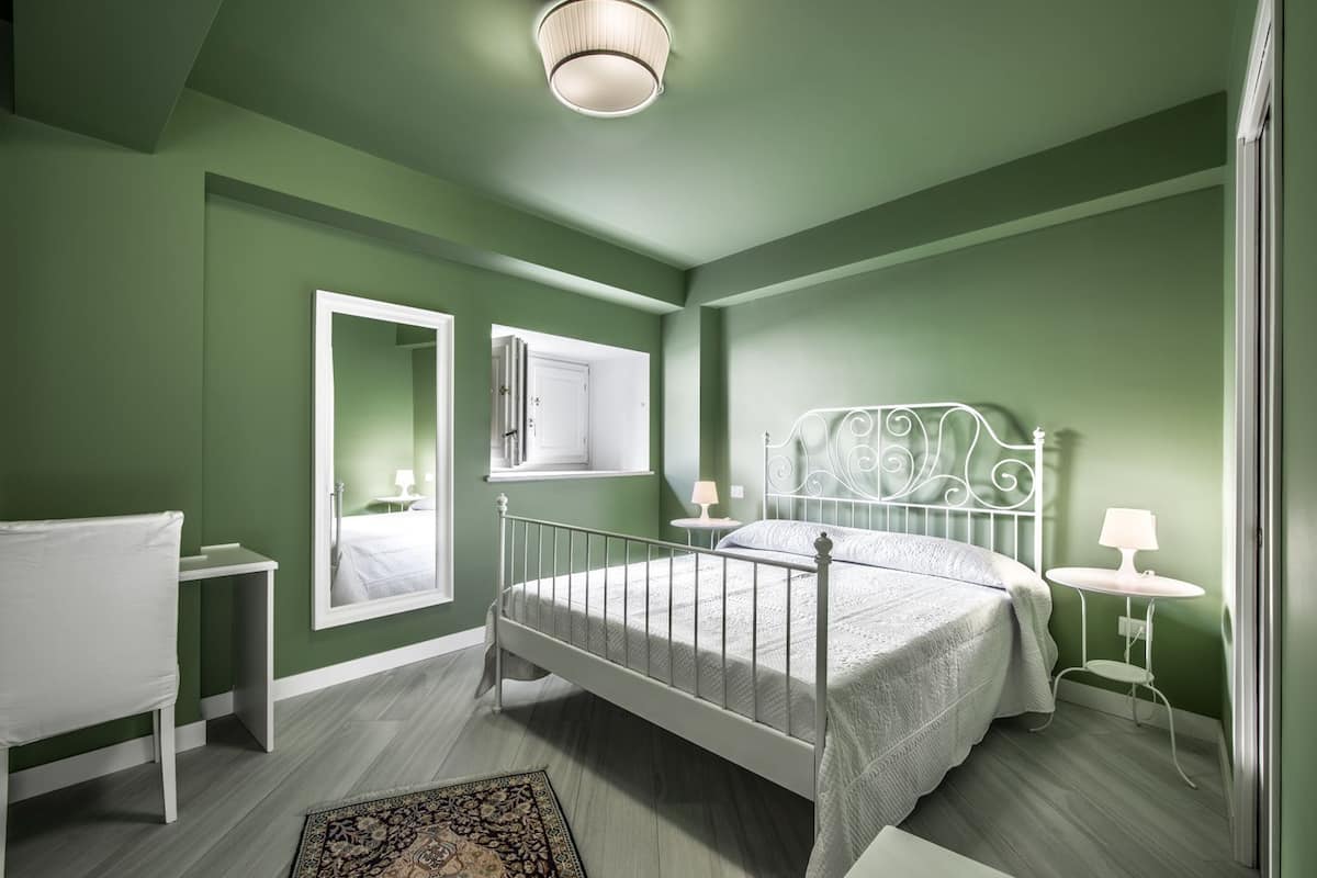 A bedroom with a bed, bedside tables, a mirror, and a window.
