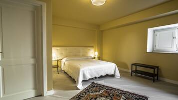 A bedroom with a bed, bedside lamps, a bench, a patterned rug, and a ceiling light.