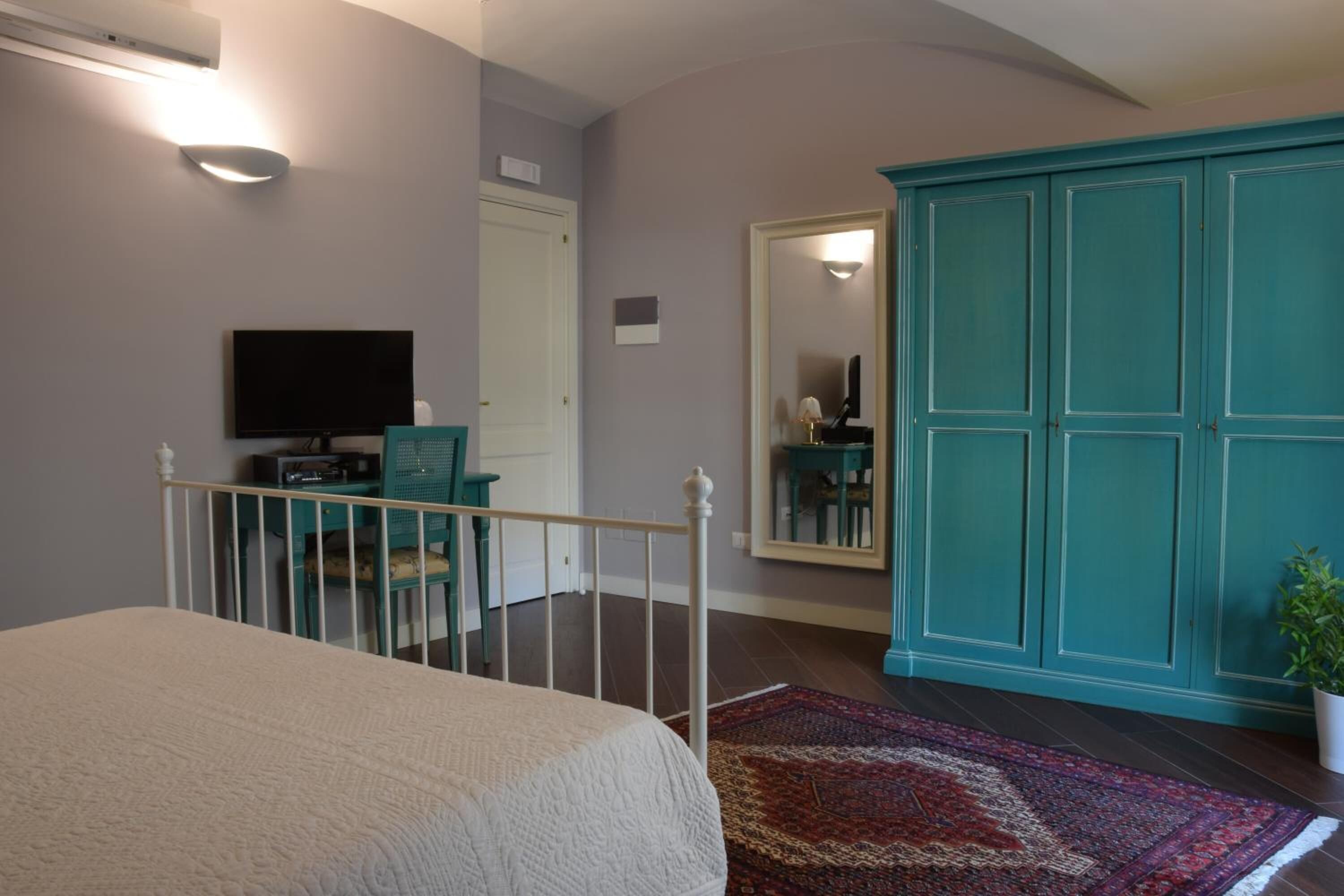 A bedroom with a bed, a desk with a chair, a television, a wardrobe, and a mirror.