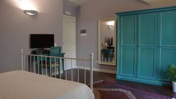 A bedroom with a bed, a desk with a chair, a television, a wardrobe, and a mirror.