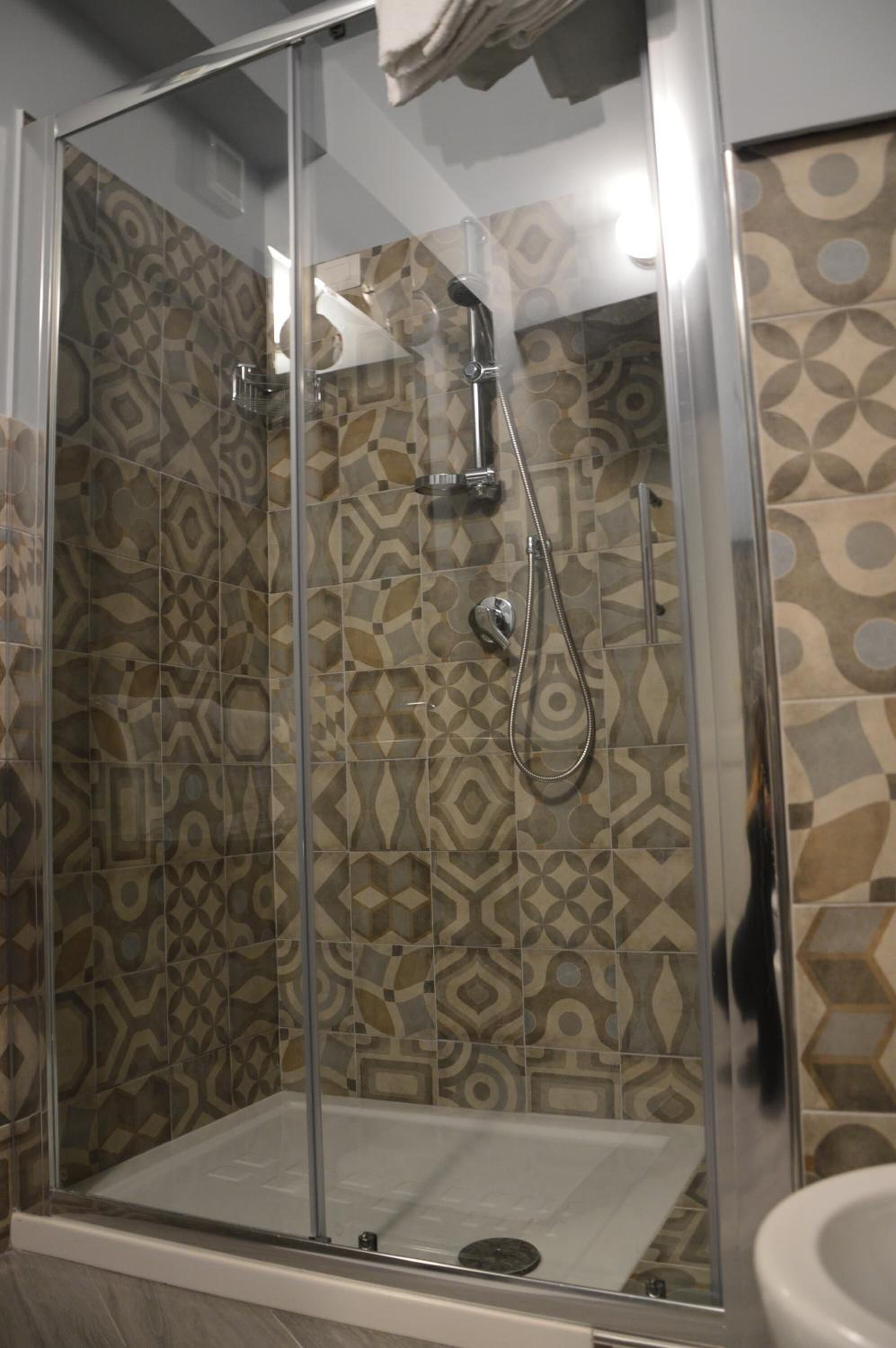 A glass-enclosed shower area with a patterned tile wall and a white sink to the right.