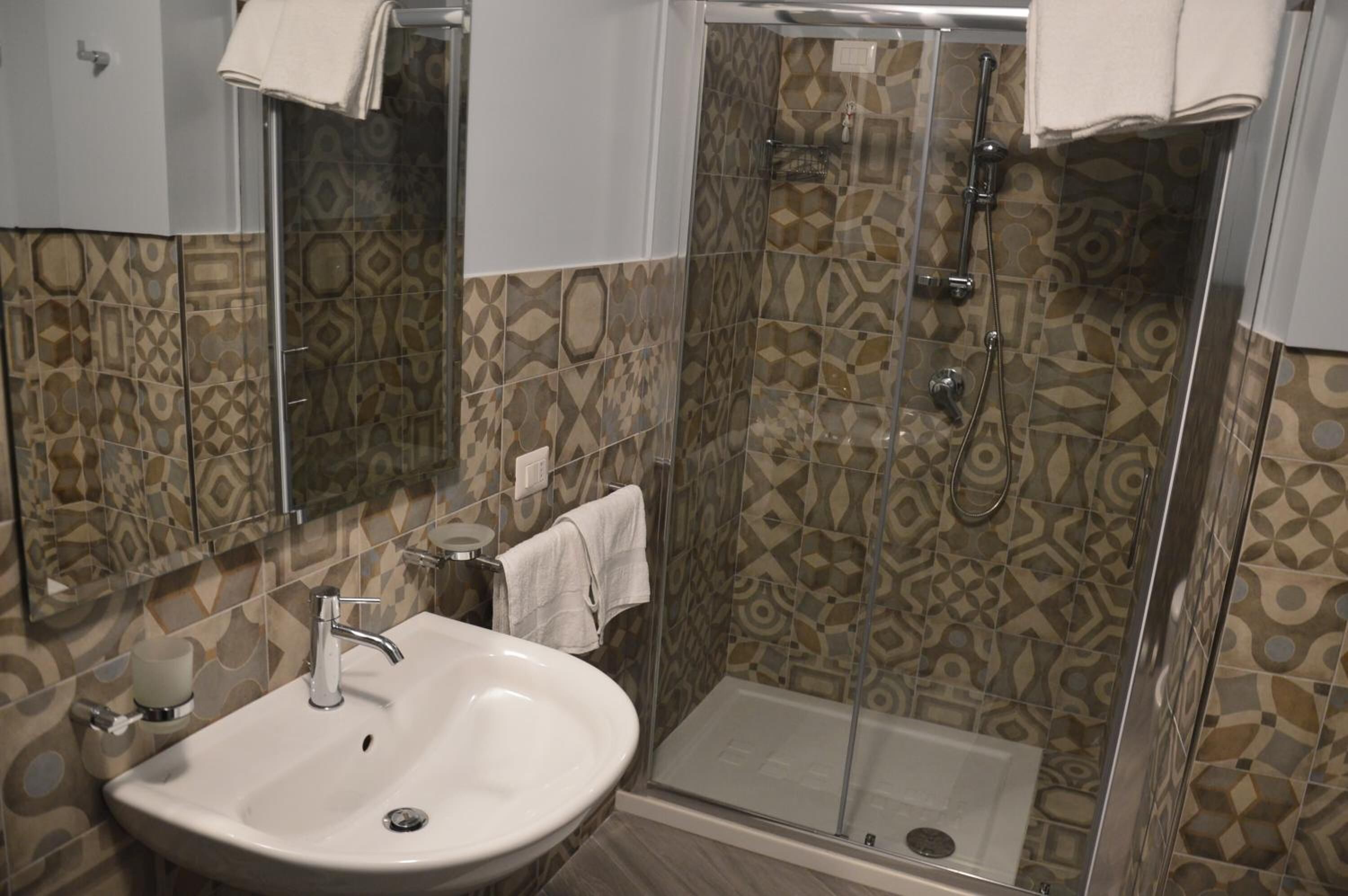 A bathroom with a shower, a sink, and patterned tiles.