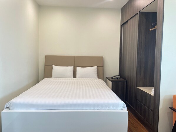 A neatly made bed with a headboard, a bedside table with a phone, and a dark wooden wardrobe.