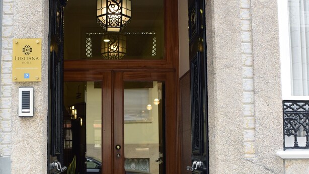 A hotel entrance with a sign reading "HOTEL" above the door, a street number "241" above the sign, and a "LUSITANA HOTEL" sign on the left.