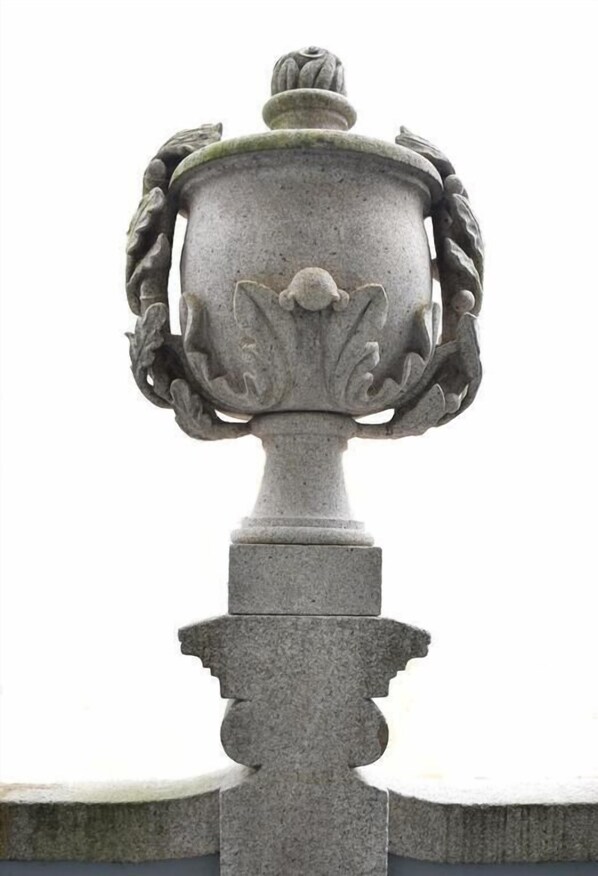 En stentørner med låg, flankeret af to dekorative løvehoveder, monteret på en pedestal.