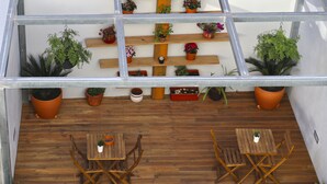 Una terraza de madera con dos mesas y sillas de madera, rodeada de plantas en macetas sobre estanterías y colgando del techo.