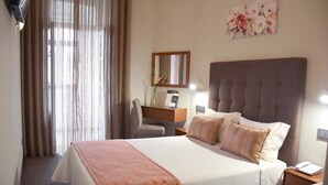 Un cuarto de hotel con una cama grande, un escritorio, una silla, un espejo y un cuadro con motivos florales en la pared.