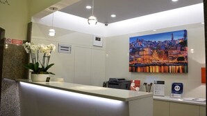 Zona de recepción de un hotel con diseño moderno, que incluye un mostrador de recepción, un cuadro grande con una vista urbana y una señal que indica la categoría del hotel.