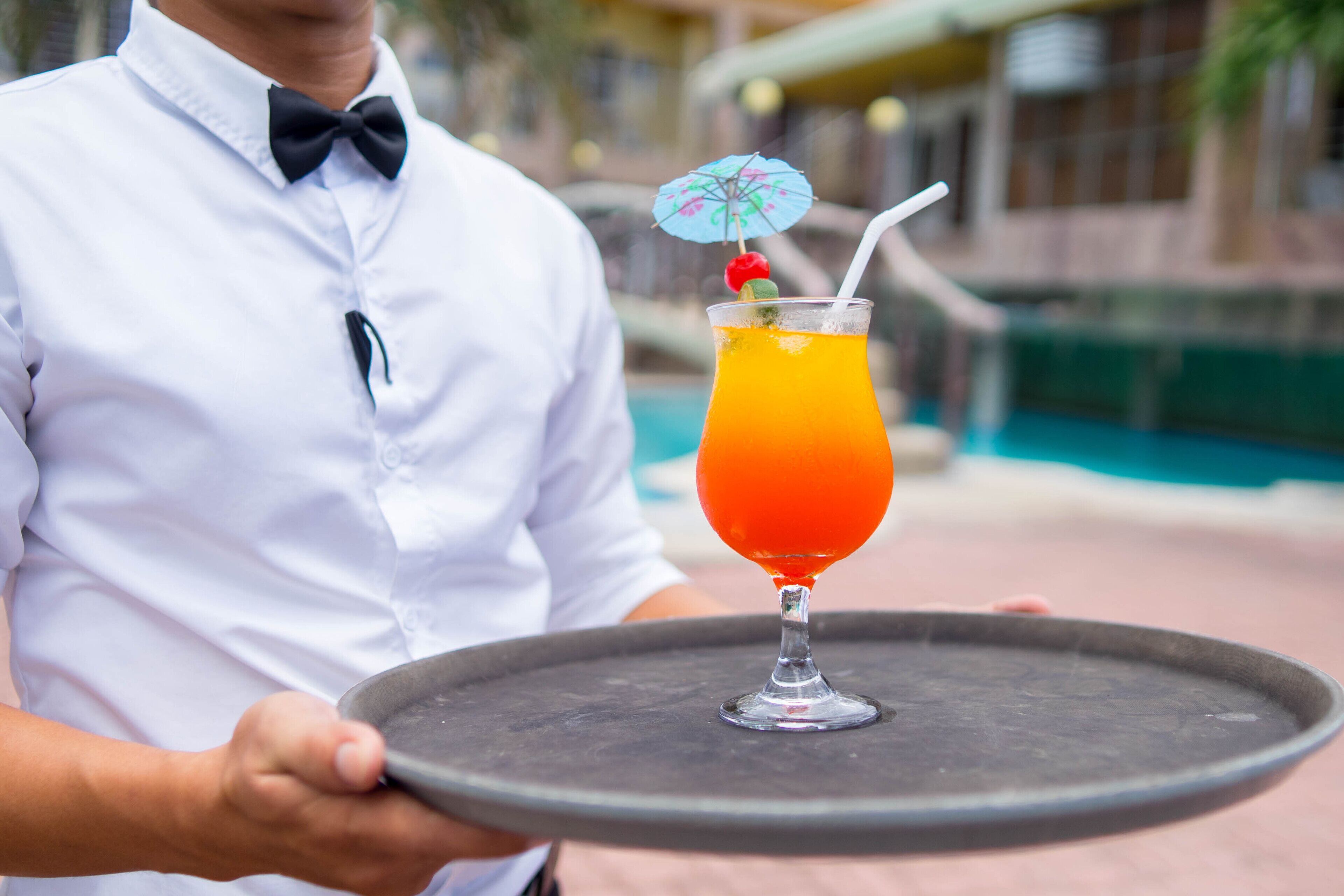 A person in a white shirt and bow tie holding a tray with a cocktail glass.