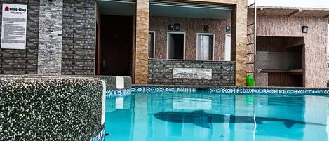 A swimming pool with a tiled edge, a stone wall, and a sign for a hotel and resort.