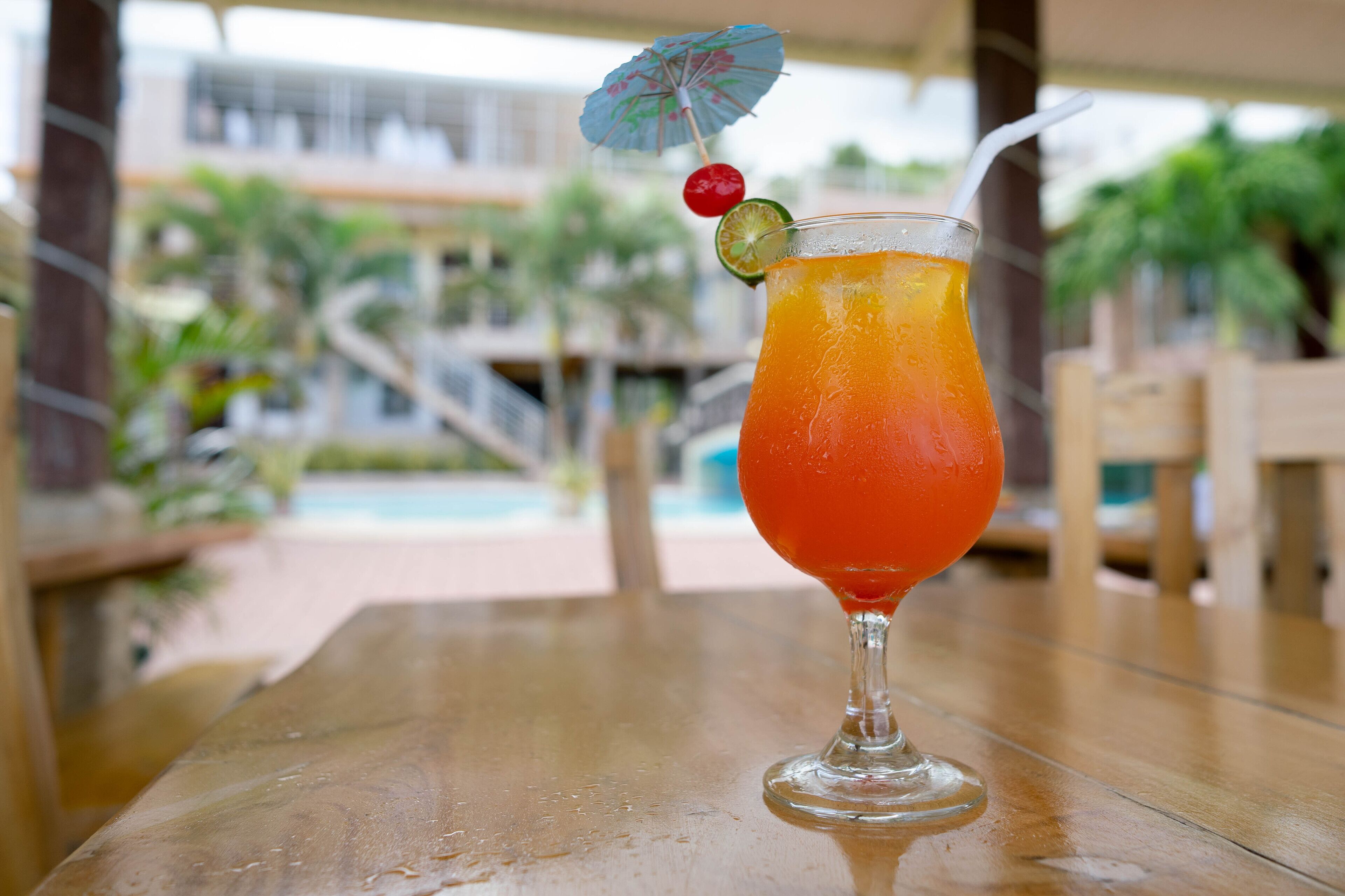 A glass of orange beverage with a lime slice and a cherry on a cocktail umbrella on a wooden table.