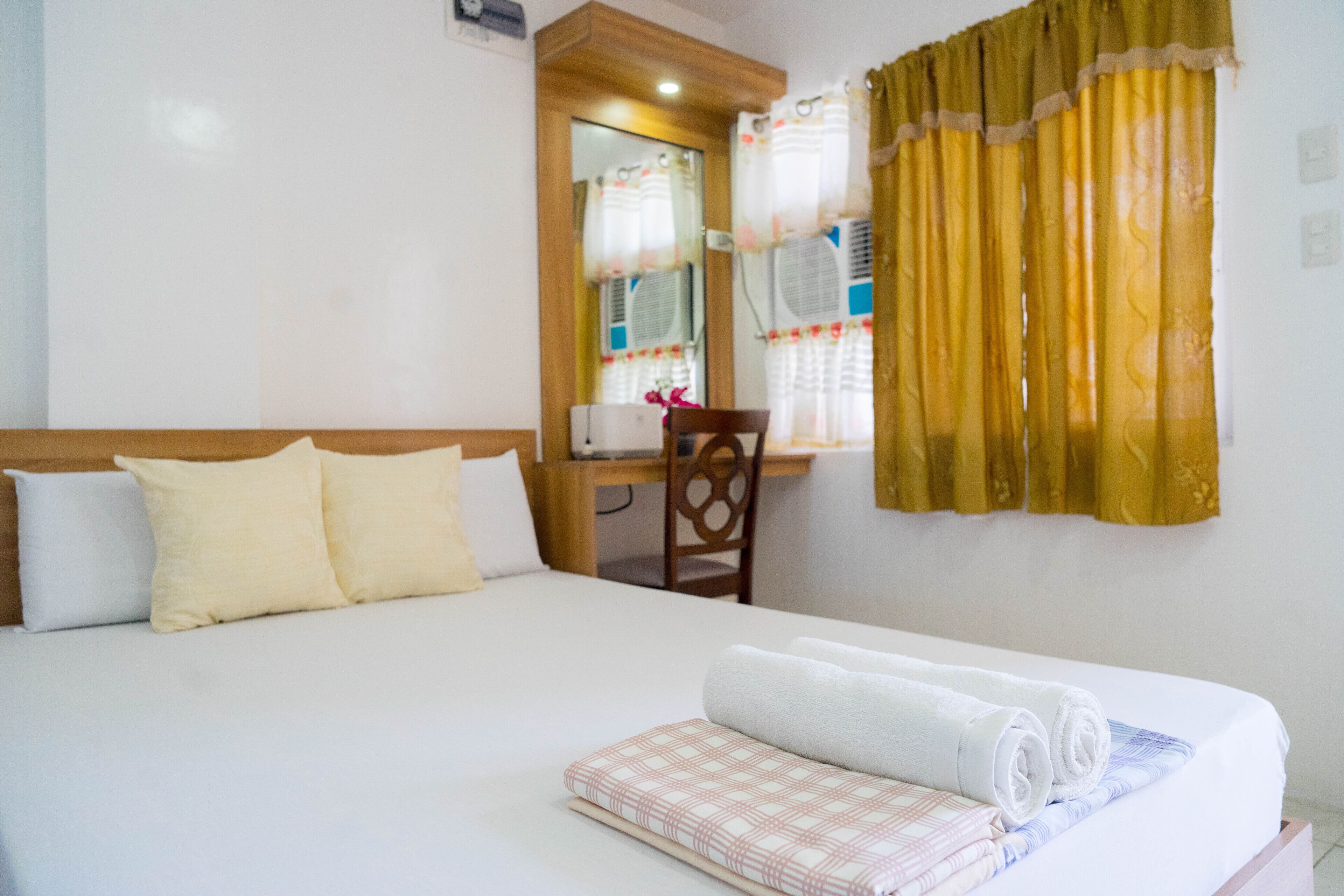 A neatly made bed with rolled towels, a wooden headboard, and a desk with a chair.