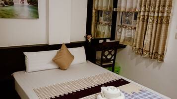 A neatly made bed with a checkered bedspread, a pair of white towels, and a decorative pillow.