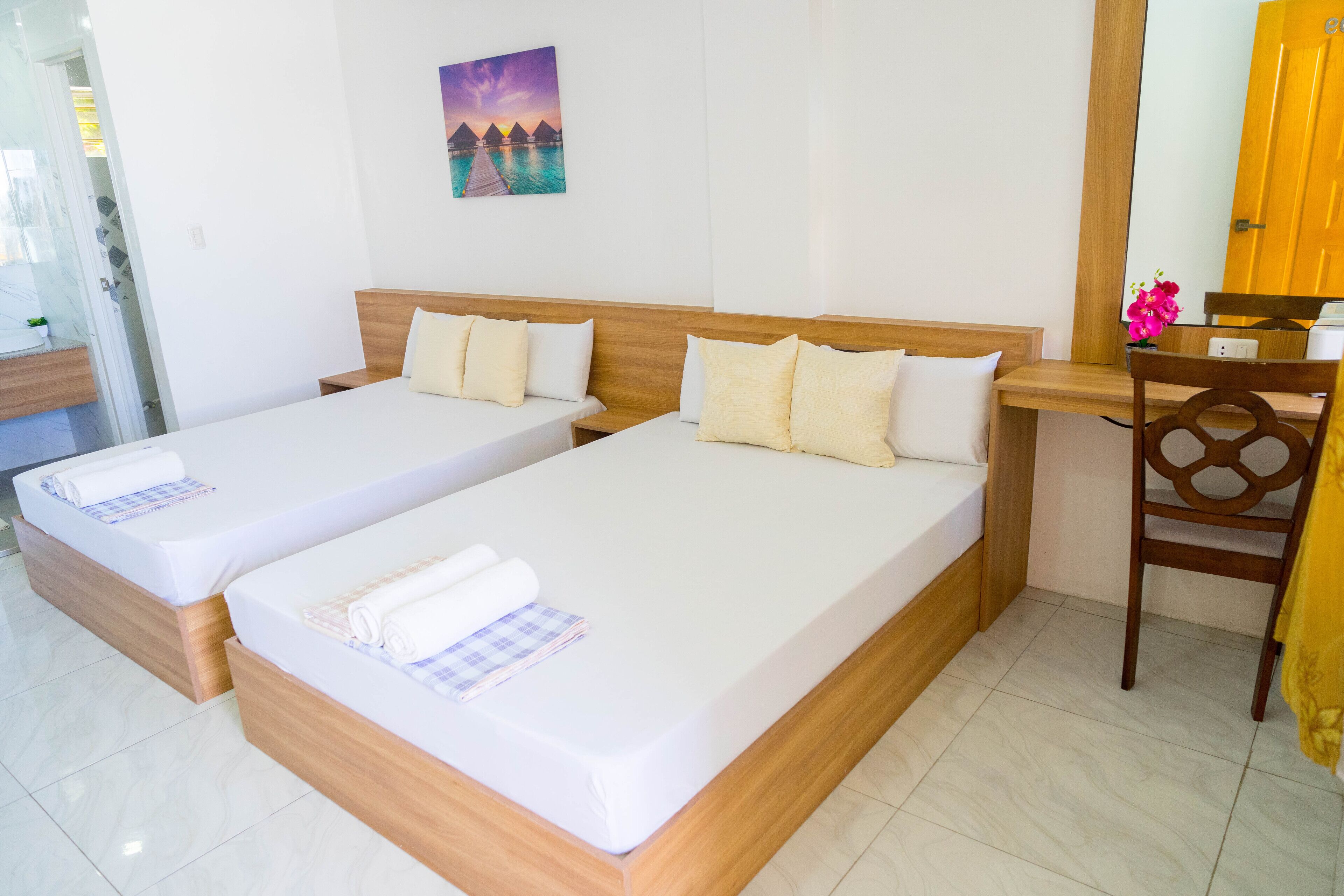 A hotel room with two single beds, a wooden desk, a chair, and a painting of a sunset over water.
