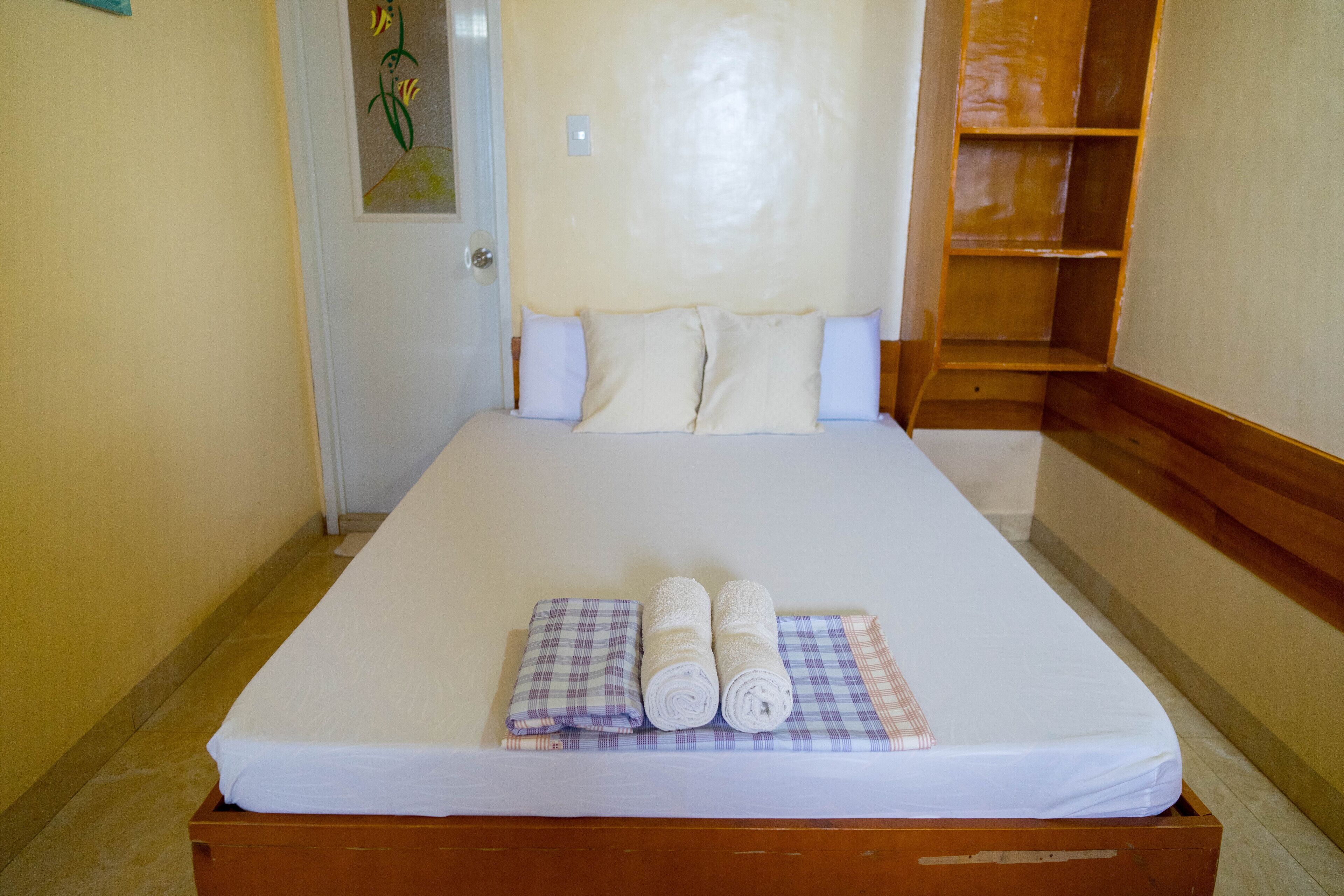 Una cama bien hecha con un colchón blanco, dos toallas enrolladas y una manta a cuadros.