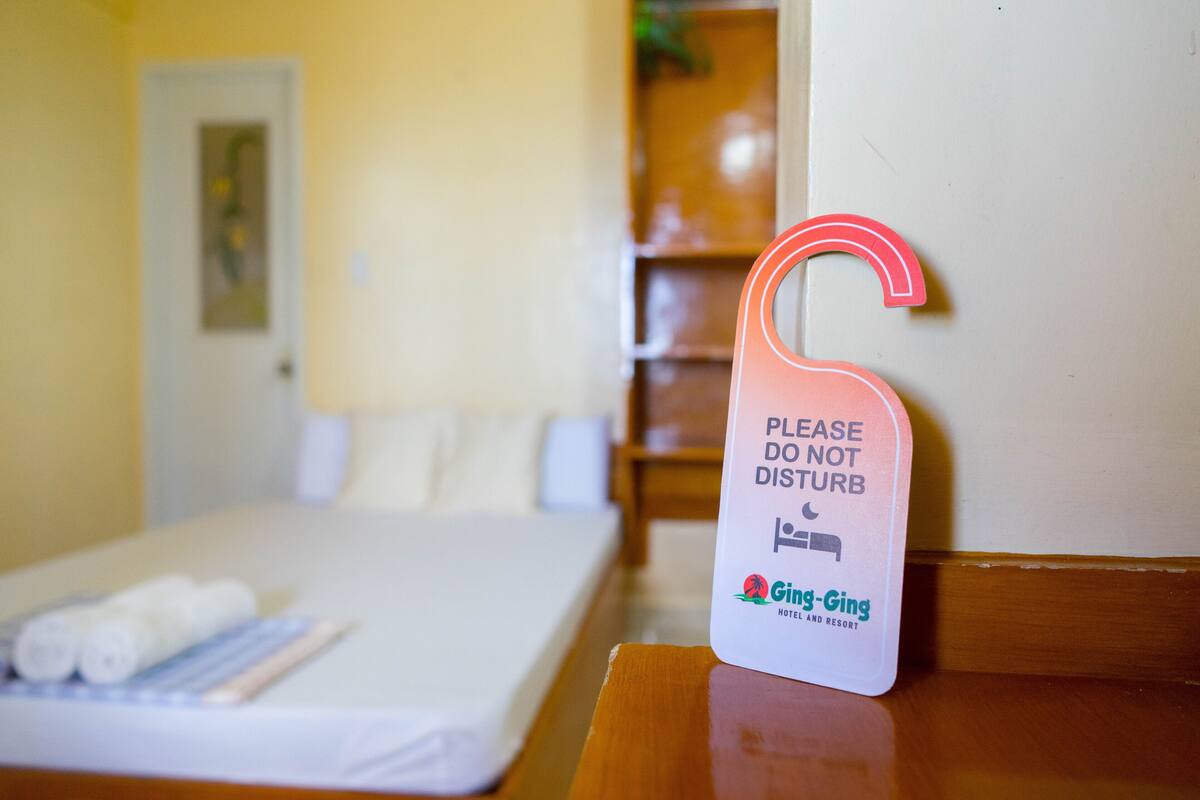 A hotel room with a bed, a bedside table, and a sign on the wall that reads "PLEASE DO NOT DISTURB."