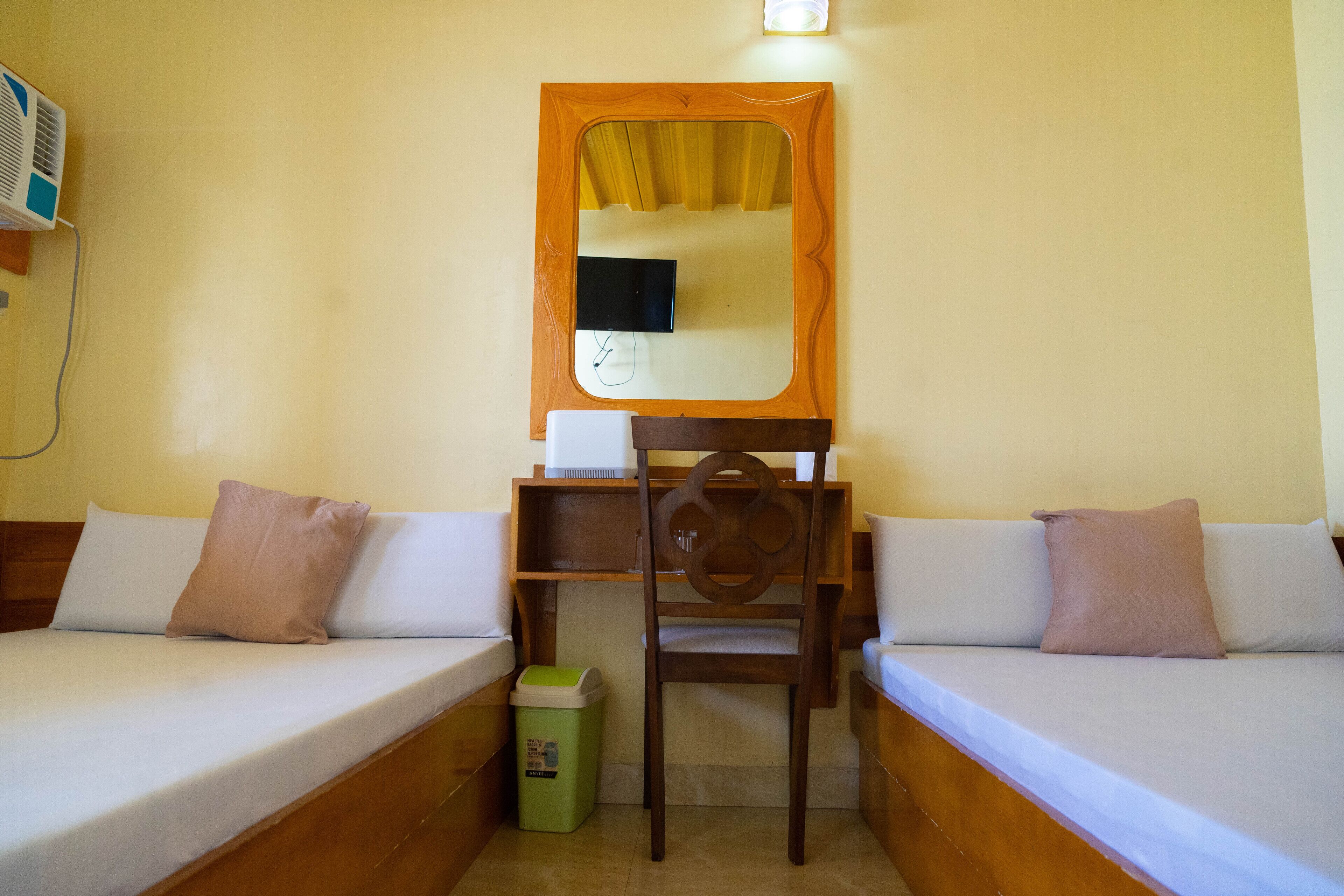 Una habitación con dos camas, un escritorio, una silla y un cubo de basura.