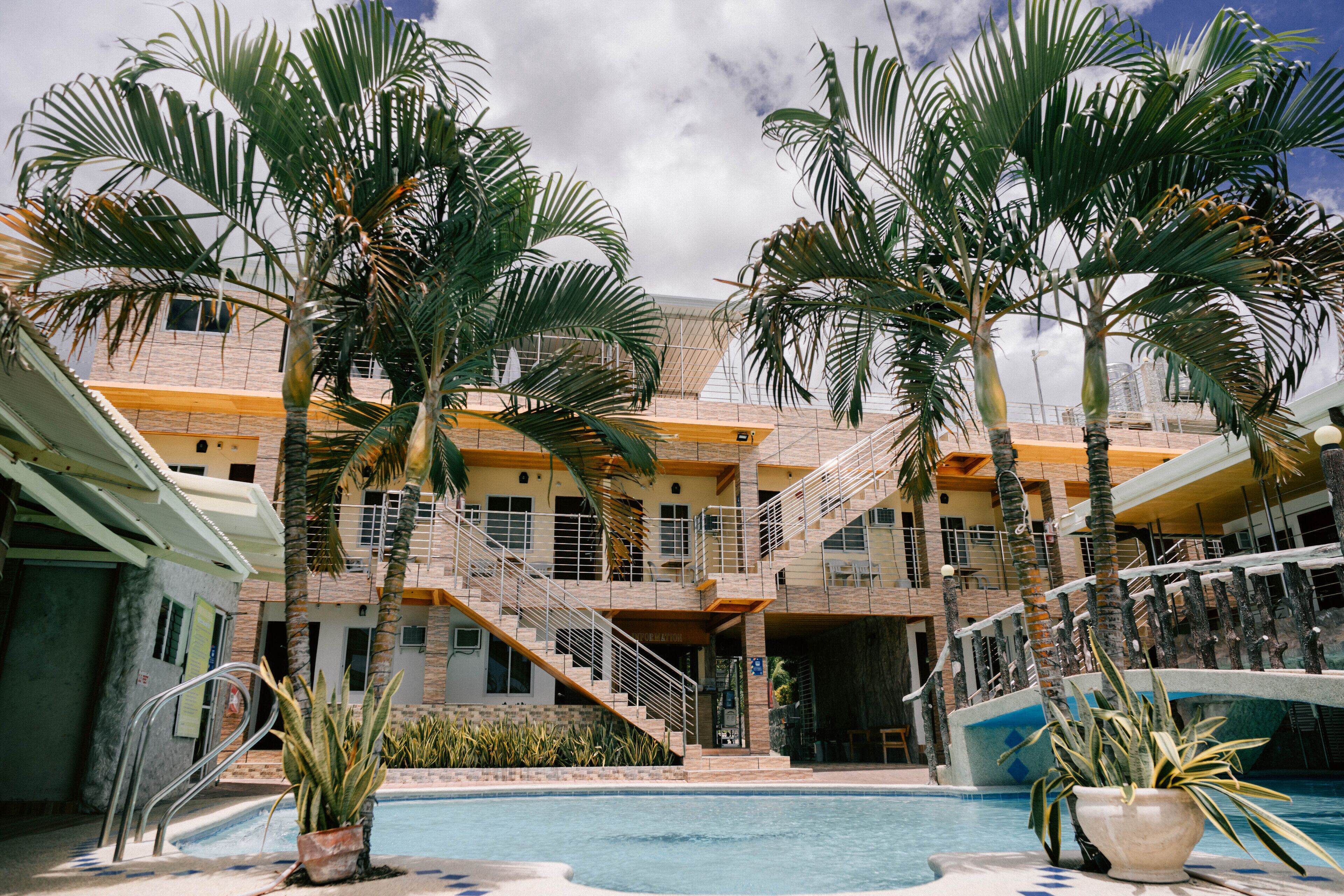 A hotel with a pool, palm trees, and a staircase leading to the upper floors.