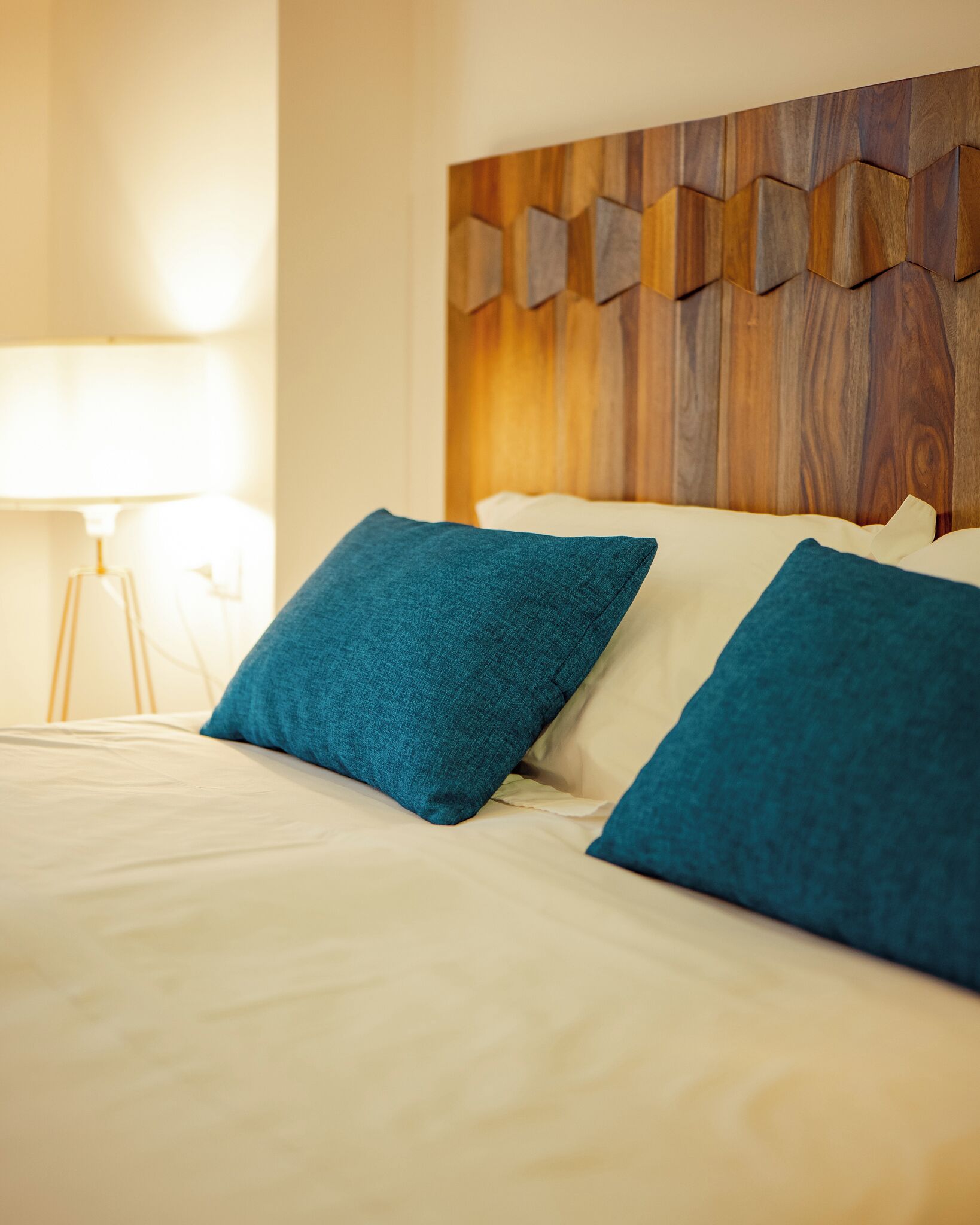 Ein ordentlich bezogenes Bett mit zwei blauen Kissen und einem Holz-Kopfbrett.