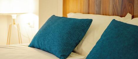 Ein ordentlich bezogenes Bett mit zwei blauen Kissen und einem Holz-Kopfbrett.