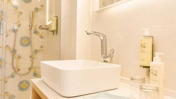 Un baño con un lavamanos blanco, una ducha con azulejos florales y artículos de aseo en la encimera.