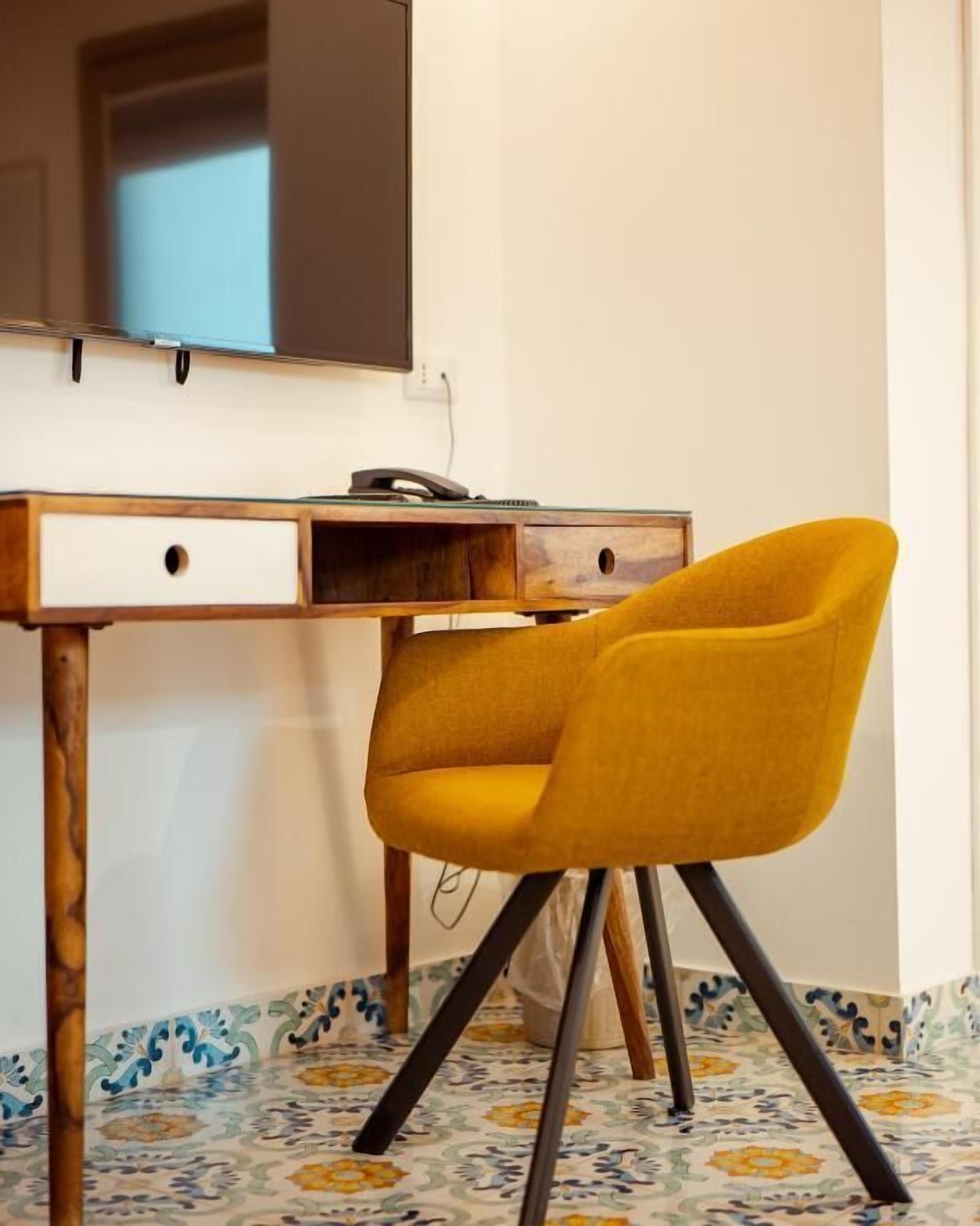 A room with a wooden desk, a yellow chair, and a tiled floor.