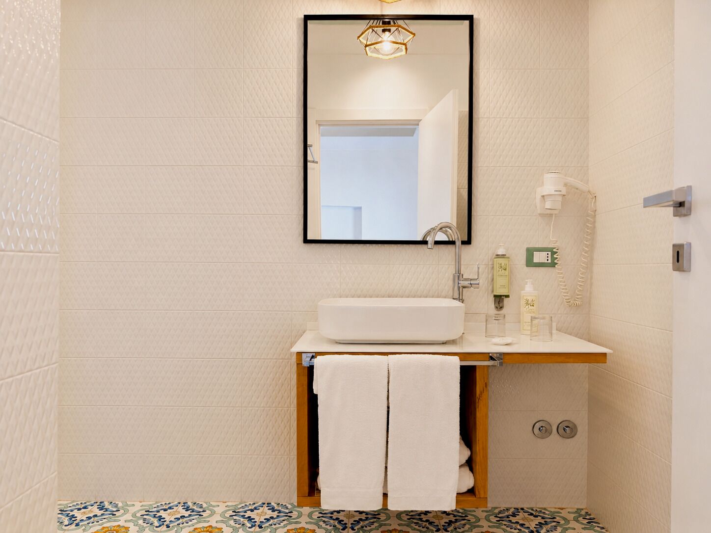 Un baño con un lavamanos blanco, un espejo, un toallero y un piso estampado.