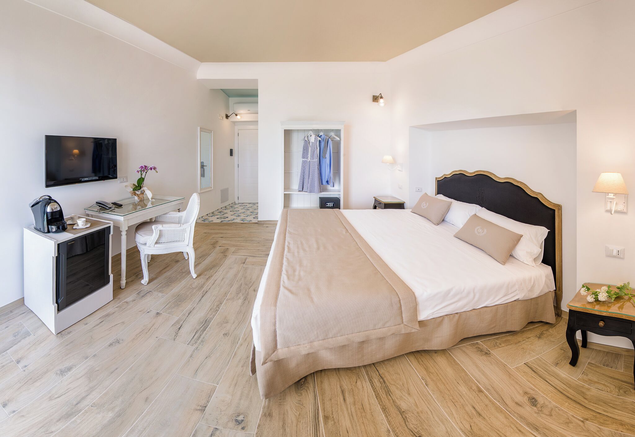 Habitación de hotel con una cama, un escritorio con televisor, una cafetera y una silla.