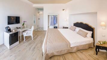 Habitación de hotel con una cama, un escritorio con televisor, una cafetera y una silla.