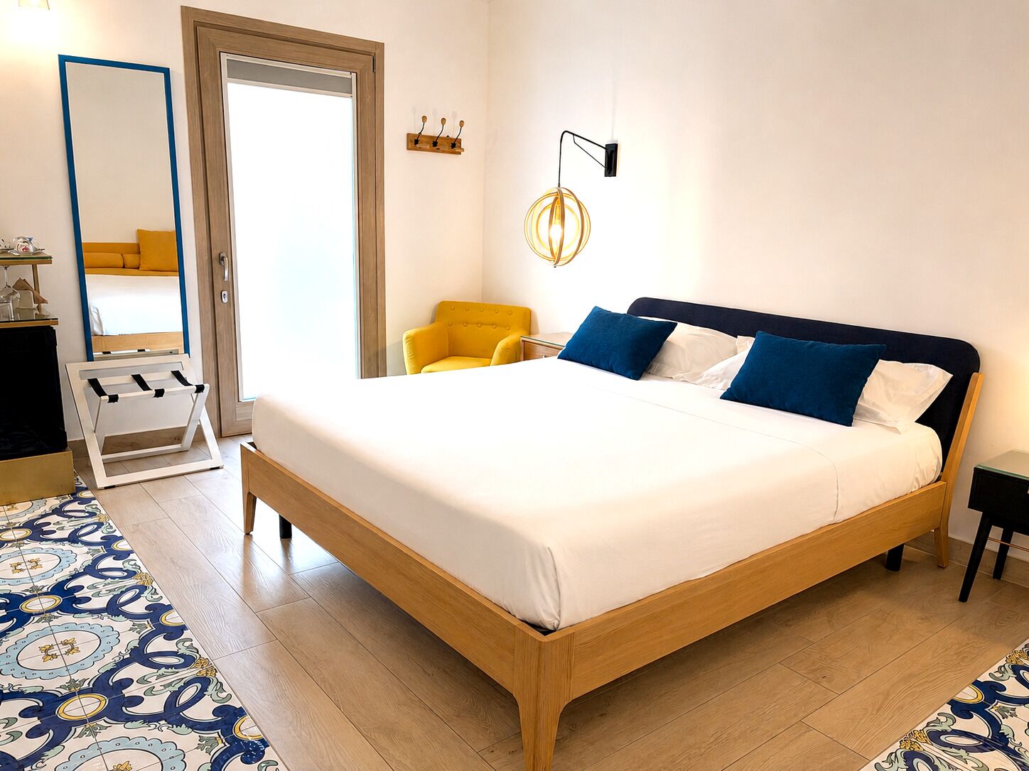 Ein Hotelzimmer mit einem hölzernen Bett, einem gelben Sessel, einem Spiegel und einem gemusterten Teppich.