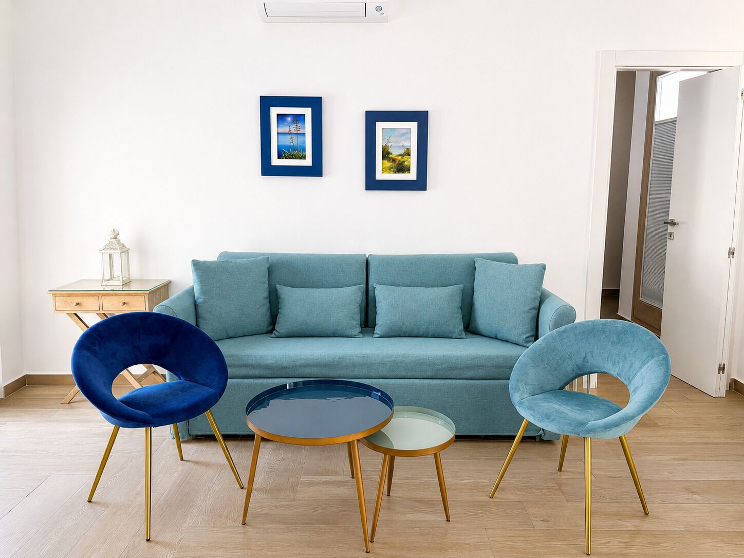 A living room with a teal sofa, two blue chairs, a small table, and two framed pictures on the wall.
