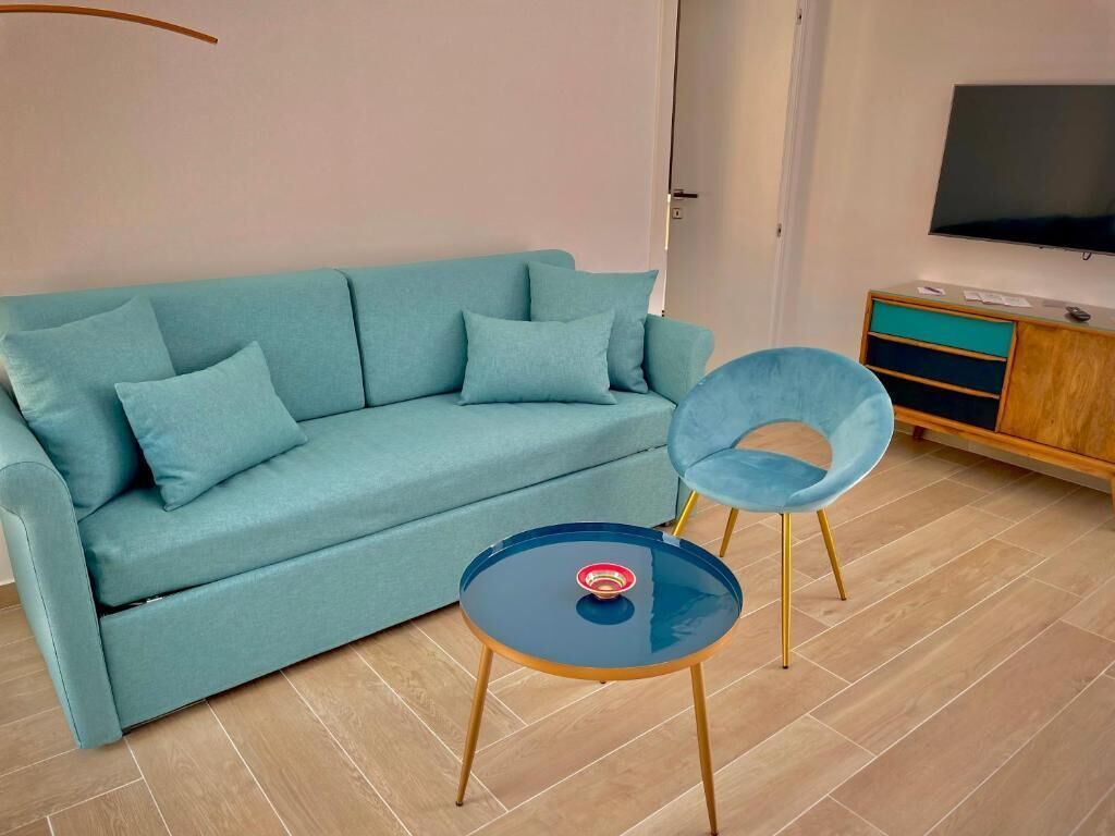 A modern living room with a teal sofa, two matching armchairs, a small round table, and a TV mounted on the wall.