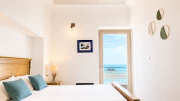 A bedroom with a bed, a nightstand, a lamp, a picture on the wall, and a door leading to a balcony with a view.