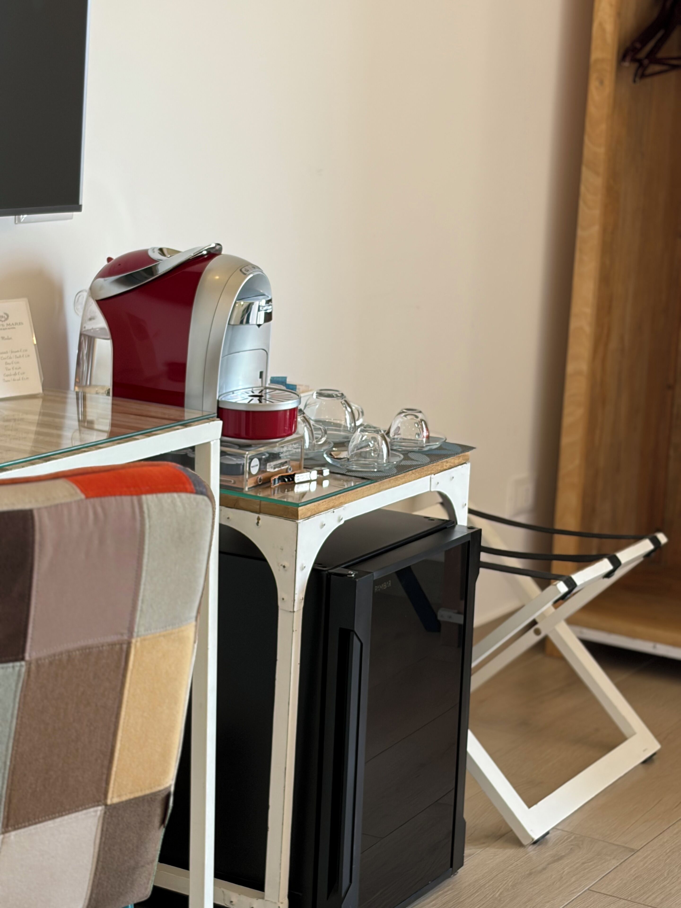 A compact kitchenette with a coffee machine, a glass-top table, and a foldable chair.