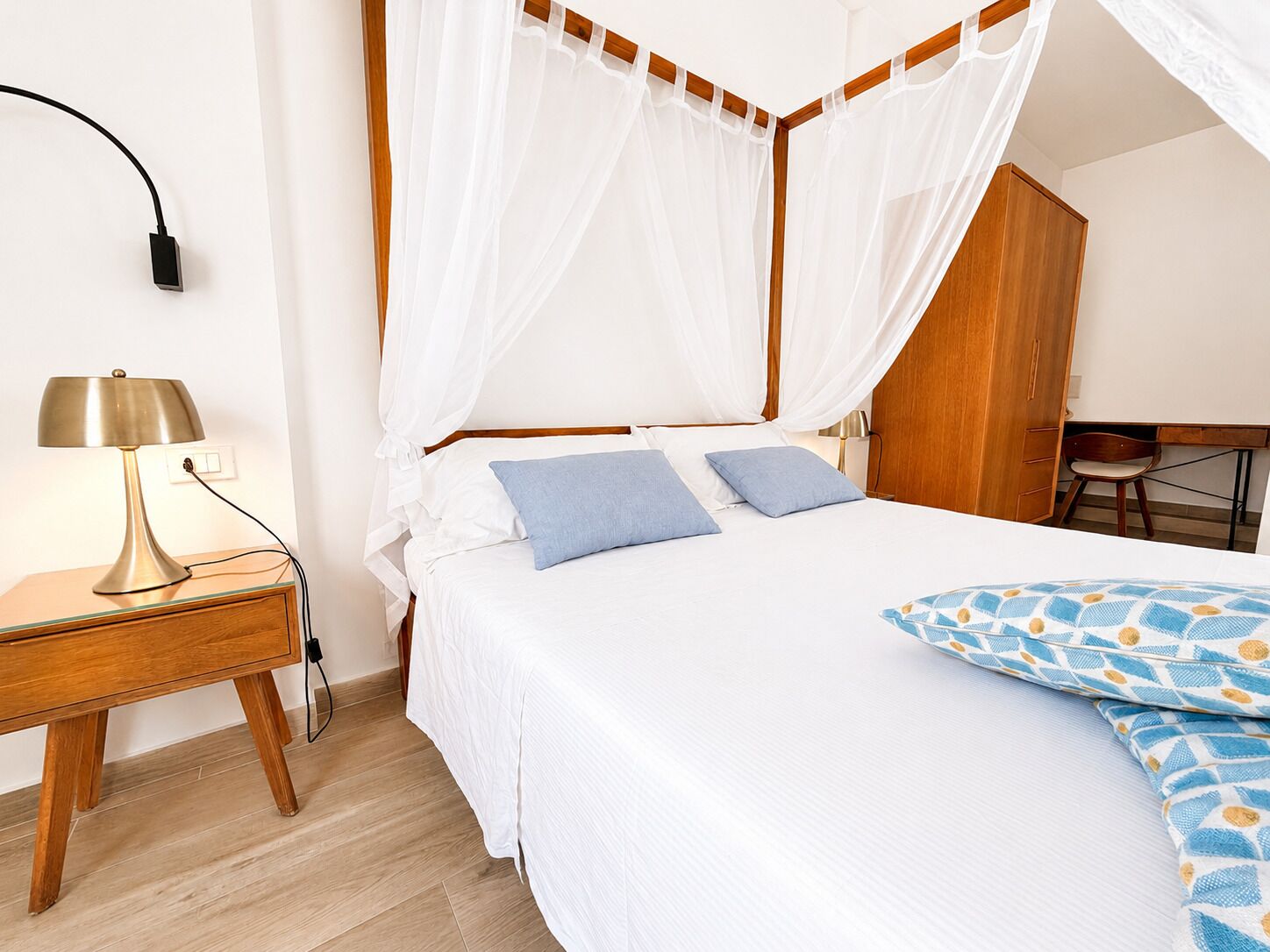 Une chambre à coucher comprenant un lit, une table de chevet avec une lampe, une armoire en bois et un bureau avec une chaise.