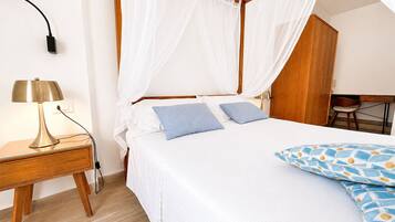 Une chambre à coucher comprenant un lit, une table de chevet avec une lampe, une armoire en bois et un bureau avec une chaise.