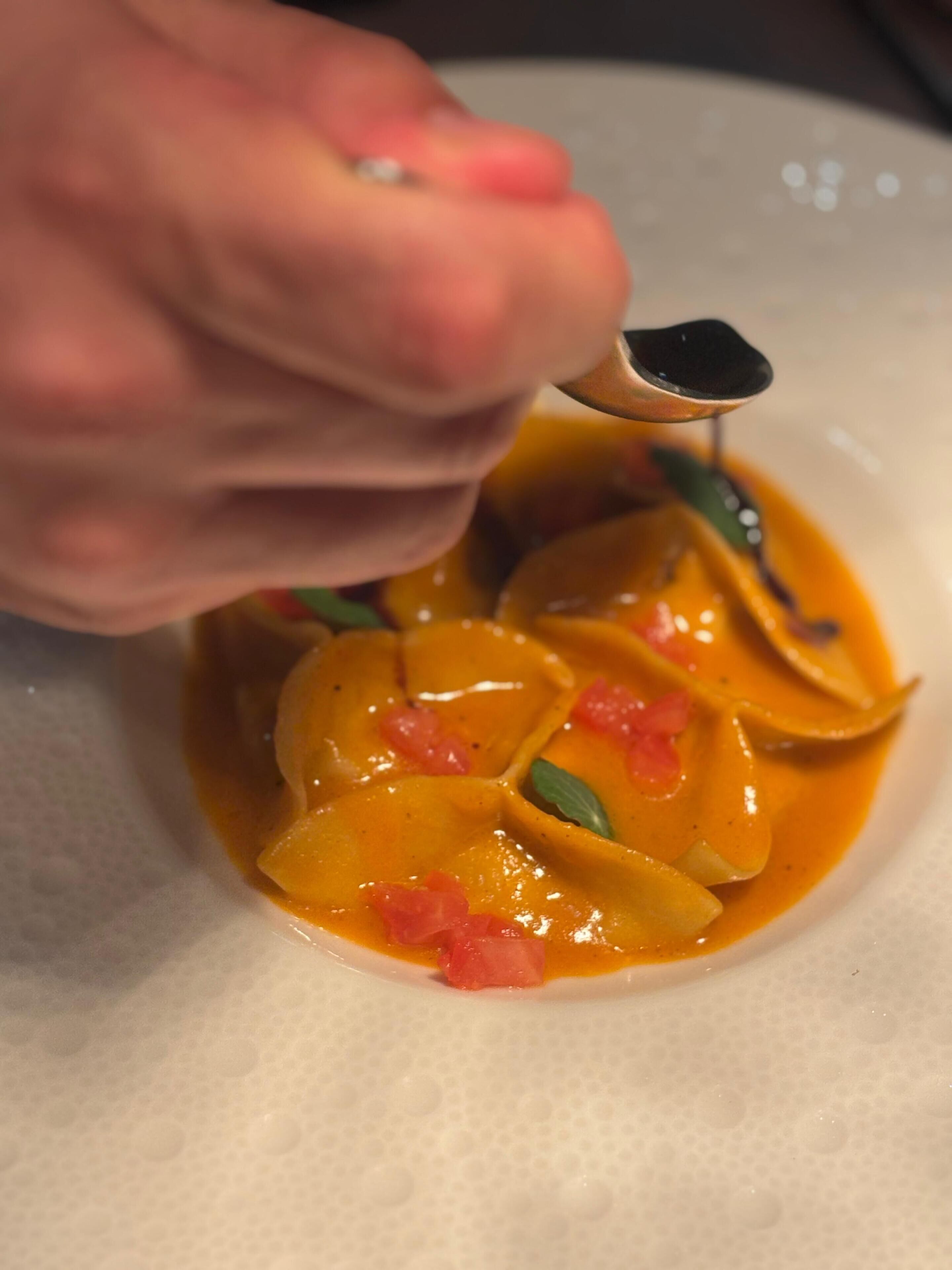 Primer plano de un plato con salsa cremosa color naranja, adornado con hojas verdes y trozos rojos, servido con una cuchara.