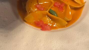 Primer plano de un plato con salsa cremosa color naranja, adornado con hojas verdes y trozos rojos, servido con una cuchara.