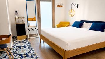 Habitación de hotel con una cama grande, una silla, una mesita, un espejo y una lámpara fijada en la pared.